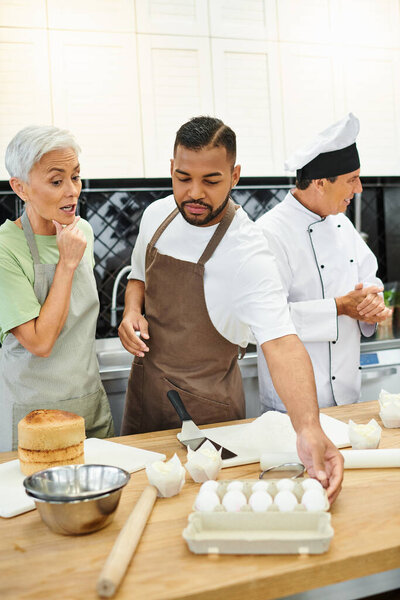 handsome african american man and mature woman baking next to chef in white hat, cooking courses