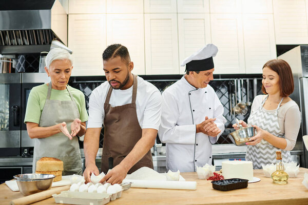 mature cheerful confectioner in white hat surrounded by his diverse students during cooking lesson
