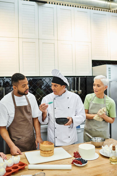 mature handsome chef in white hat teaching how to bake his diverse students, cooking courses