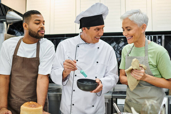cheerful mature woman and african american man learning how to bake with jolly chef, cooking courses