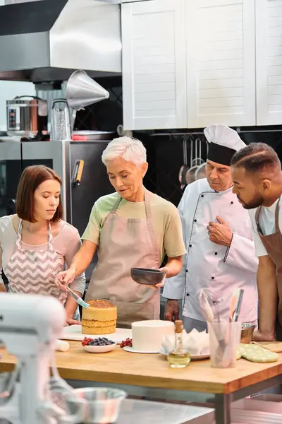 mature woman in apron brushing cake with syrup on cake next to diverse friends and chef in white hat