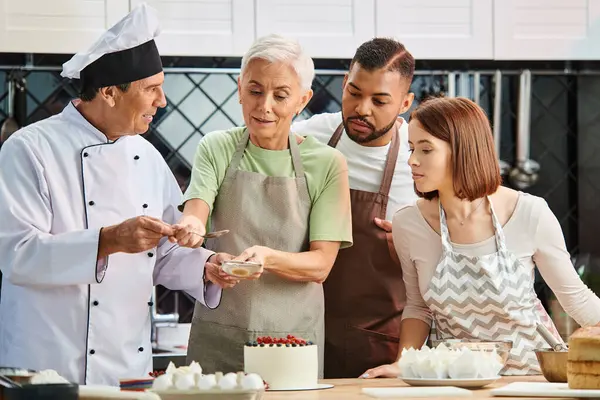 mature jolly chef smiling at woman decorating cake next to his other students, cooking courses