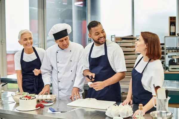 stock image joyous african american male chef breaking egg and smiling happily at his colleagues and chief cook