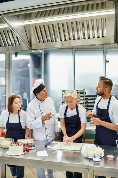 Stock image good looking jolly diverse confectioners in aprons baking delicious cakes with chef in white hat