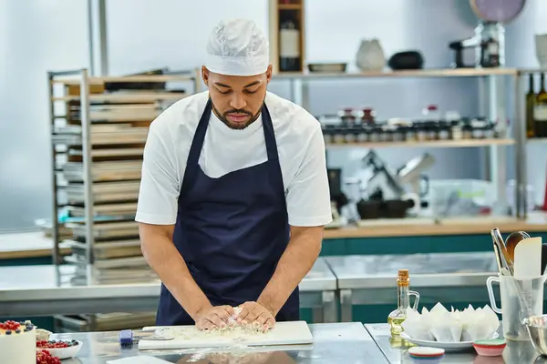 good looking african american chef in blue apron working with dough on kitchen, confectionary
