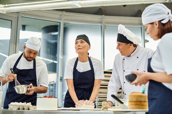 good looking mature chief cook talking to his hard working interracial chefs while on kitchen