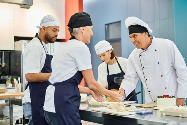 happy mature chief cook and chef smiling while their interracial colleagues working on pastry