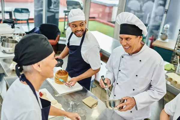 jolly multiracial team on chefs in blue toques looking at their mature chief cook, confectionery