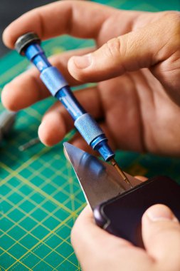 partial view of technician opening smartphone with screwdriver during testing in own workshop clipart