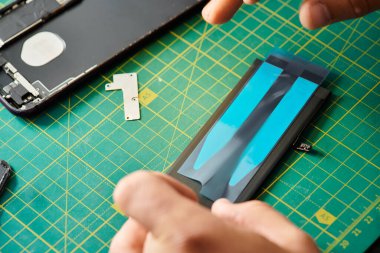 cropped view of technician working with battery of mobile phone in repair shop, repair service clipart