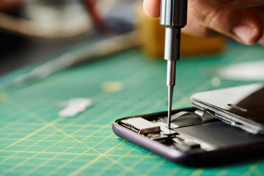 Tornavida ile açarken cep telefonunu test eden tamircinin kırpılmış görüntüsü, küçük işletme