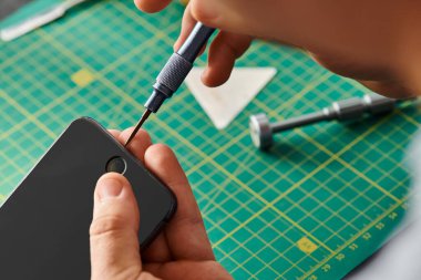 cropped view of experienced technician opening smartphone with screwdriver in private workshop clipart