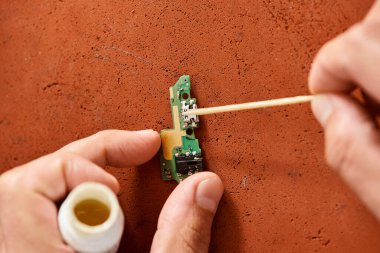 cropped view of professional technician cleaning electronic microscheme working in own workshop clipart