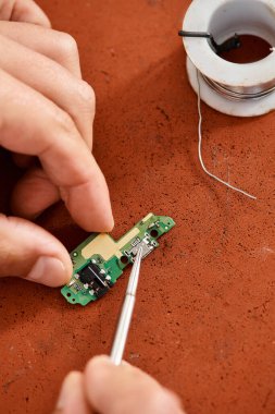 Cımbızla atölyede elektronik çipleri test eden profesyonel tamirci görüntüsü.