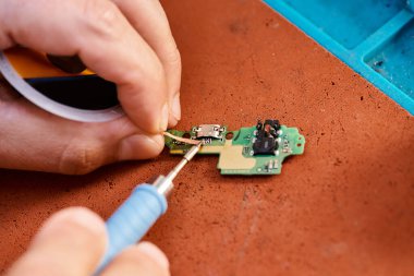 Tamir atölyesinde elektronik mikro şemayı lehimleyen teknisyenlerin kısmi görüntüsü, bakım servisi