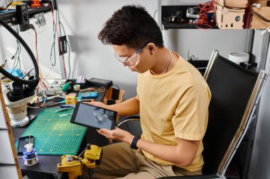 Asyalı teknik gözlük uzmanı. Kırık dokunmatik ekranlı dijital tableti inceliyor.