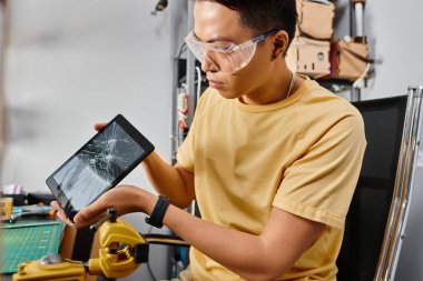 Gözlüklü profesyonel Asyalı tamirci, dokunmatik ekranlı dijital tablete bakıyor.