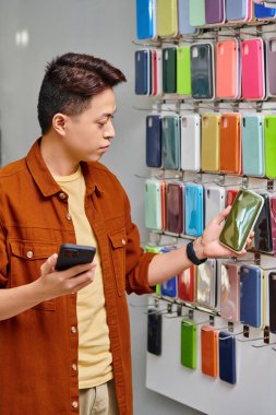 Akıllı telefonlu Asyalı bir dükkan sahibi özel bir mağazada telefon kulübesine bakıyor, küçük bir işletme.