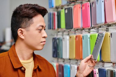 Asyalı girişimci renkli telefon kulübesine bakıyor. Özel mağaza vitrini, küçük işletme.