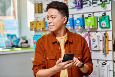 Memnun Asyalı girişimci cep telefonu tutuyor ve özel elektronik mağazasına bakıyor.