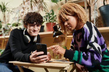 Kıvırcık saçlı mutlu çift rahat bir vejetaryen kafede akıllı telefondan menü seçiyor.