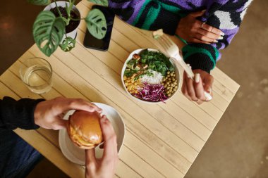 top view of young and diverse couple enjoying vegan meal in cafe, burger with tofu and salad clipart