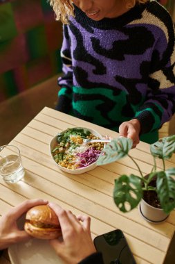 overhead view of african american woman with braces enjoying salad bowl near man with vegan burger clipart