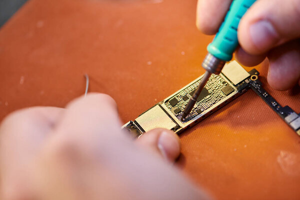 close up view of cropped technician assembling chipset by soldering in repair shop, small business