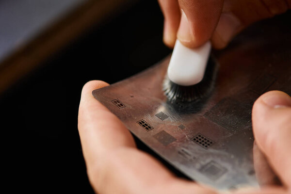 cropped view of technician cleaning electronic circuit with brush while working in repair shop