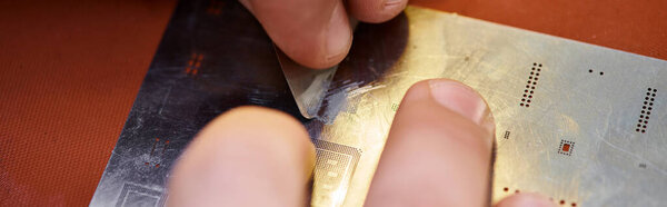cropped view of repairman scratching electronic microscheme during diagnostics in workshop, banner