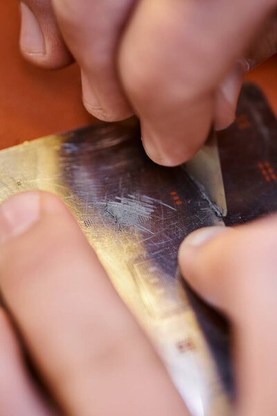 cropped repairman scratching electronic chipset during testing in workshop, small business