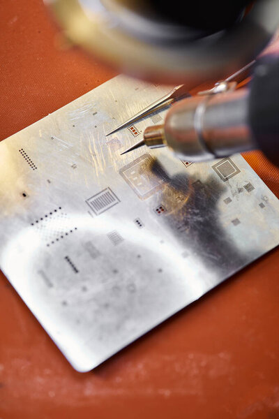 close up view of tweezers and soldering iron near chipset of electronic device in workshop