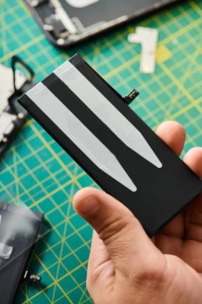 stock image cropped view of skilled technician holding battery of smartphone during testing in repair shop