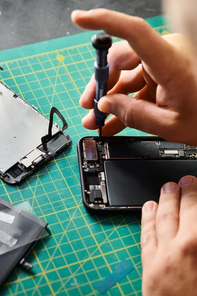 partial view of technician using screwdriver on mobile phone in professional repair workshop