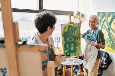 Sanat stüdyosunda resim sehpasında birbirine bakan neşeli olgun kadınlar, sanatsal yaratıcı hobi.