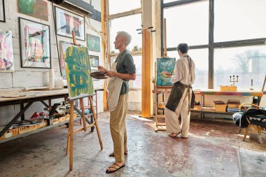Modern sanat atölyesinde resim yapan olgun ve yaratıcı kadınların duvarlarında renkli resimler var.
