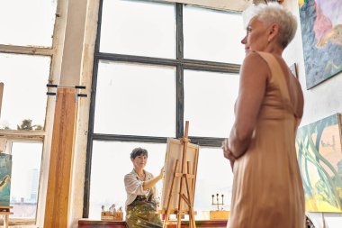 Atölyede kadın ressamın yanında poz veren şık orta yaşlı model, sanatsal süreç