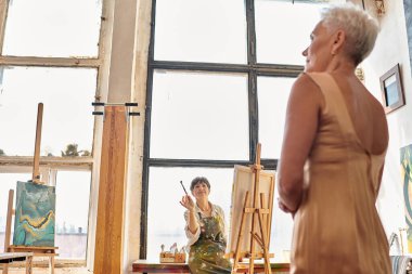 Profesyonel olgun kadın sanatçı sanat atölyesinde modelle konuşuyor, yaratıcı süreç.