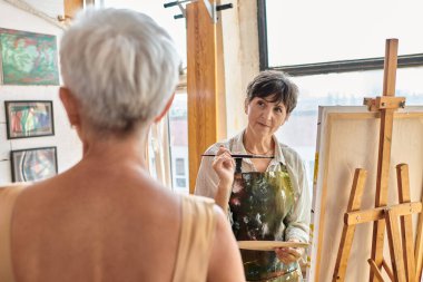 Sanat atölyesinde bulanık olgun modele bakan konsantre kadın sanatçı, yaratıcı süreç