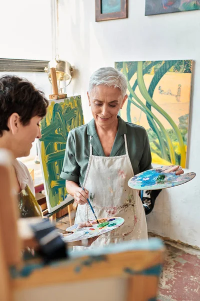 creative female friends with color palettes in modern painting studio, creative art and friendship