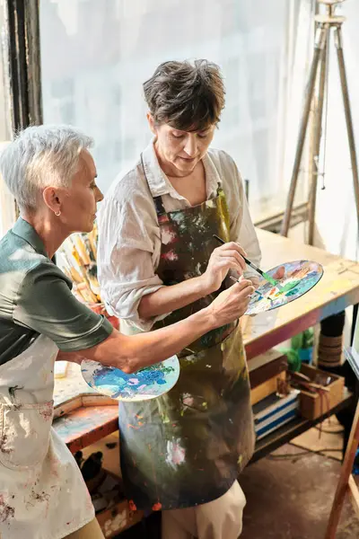Sanat atölyesinde yüksek lisans yaparken palette renk karıştıran olgun kadın sanatçılar, yaratıcı hobi.
