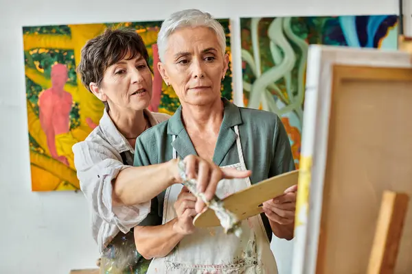 stock image skilled female artist pointing at easel near mature woman during master class in art workshop