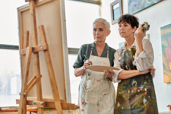 вдумчивые и творческие зрелые женщины, смотрящие на мольберта во время мастер-класса живописи в художественной мастерской