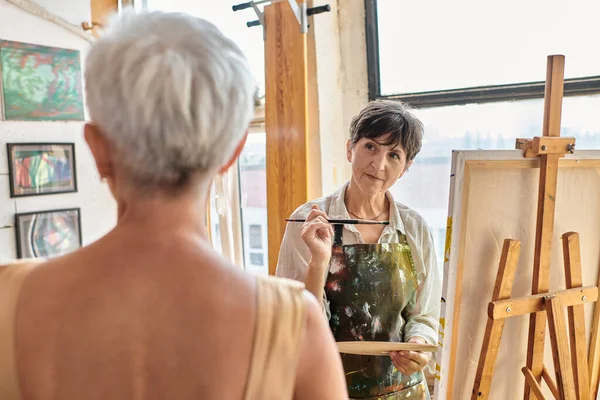 Sanat atölyesinde bulanık olgun modele bakan konsantre kadın sanatçı, yaratıcı süreç