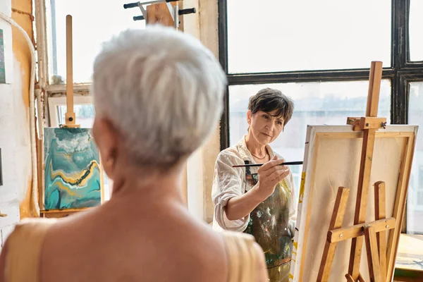 skilled female artist painting blurred mature model in art workshop, talent and creativity