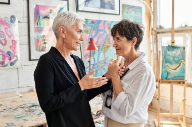 Modern sanat atölyesinde, takım çalışmasında konuşan mutlu ve şık lezbiyen çift.
