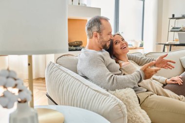 Mutlu çift evdeki modern oturma odasında rahat koltukta konuşuyor, çocuksuz bir yaşam tarzı.