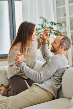 Neşeli, çocuksuz çift el ele tutuşuyor ve kanepede birbirlerine gülüyorlar. Oturma odasında uyum içinde.