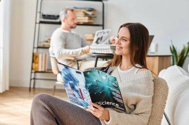 Oturma odasında kocasının yanında fen dergisi okuyan gülümseyen kadın, çocuksuz bir çiftin boş vakitleri.