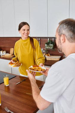 caring wife giving delicious breakfast to husband with orange juice in kitchen, child-free couple clipart